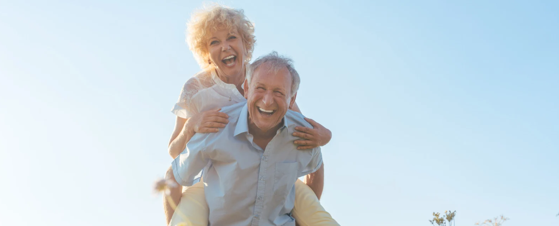 casal de idosos sorrindo ao ar livre representando qualidade de vida e bem-estar na terceira idade