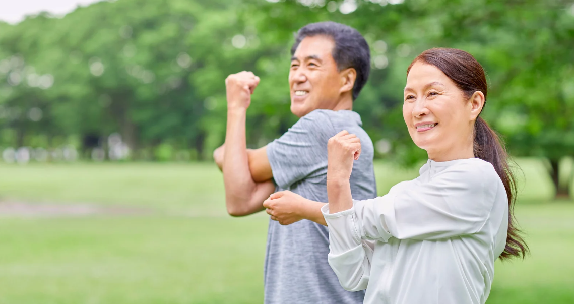 casal de idosos fazendo alongamento em parque representando saúde e envelhecimento ativo