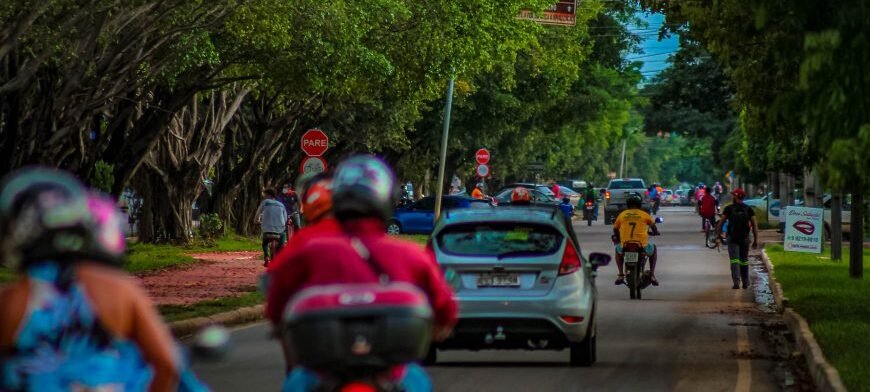 Trânsito com motos e carros circulando em rua arborizada de Ariquemes em Rondônia