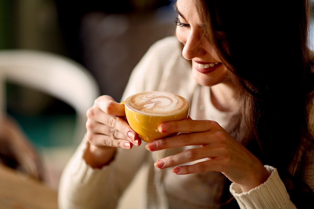 Mulher sorrindo segura xícara de café no Dia Mundial do Café