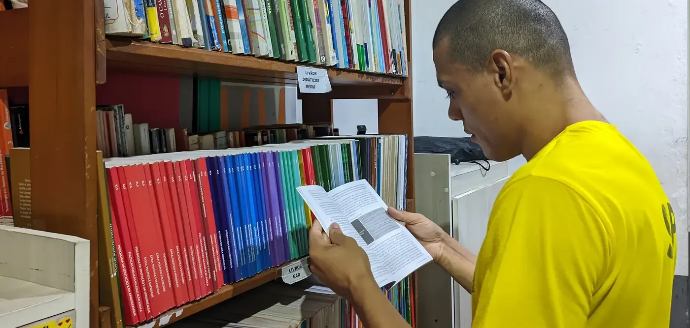 Homem lendo livro em biblioteca.