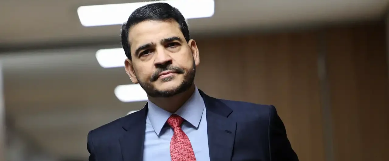 Jorge Messias caminhando em corredor institucional com documentos em mãos antes de sabatina no Senado