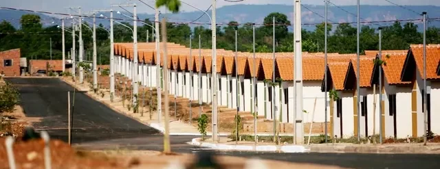 Conjunto habitacional com fileiras de casas populares e postes de energia em área urbana