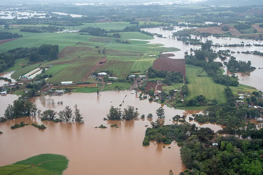 Área rural alagada no Rio Grande do Sul mostra lavouras, casas e estradas atingidas pelas enchentes.