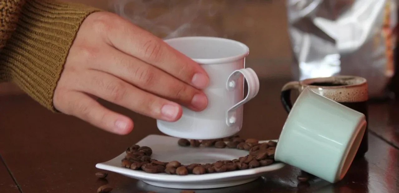 Mão segura xícara de café quente com grãos sobre a mesa no Dia Mundial do Café