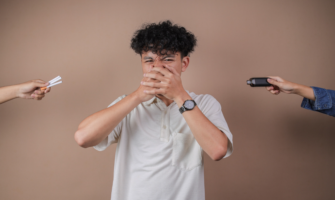 Jovem cobre o nariz e a boca enquanto recebe oferta de cigarro e vape, em imagem sobre prevenção ao tabagismo.