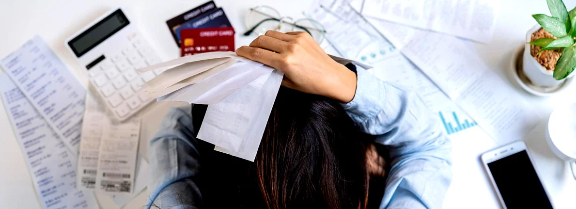 Pessoa sobre mesa com contas, cartões e calculadora em cenário de endividamento familiar