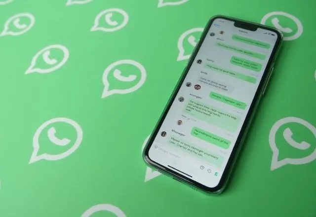 Celular com conversa no WhatsApp sobre fundo verde com ícones do aplicativo