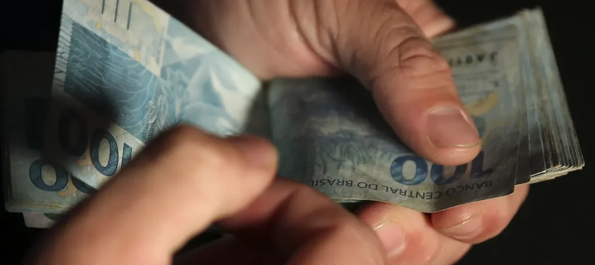 Mãos contando notas de cem reais em meio ao endividamento das famílias brasileiras