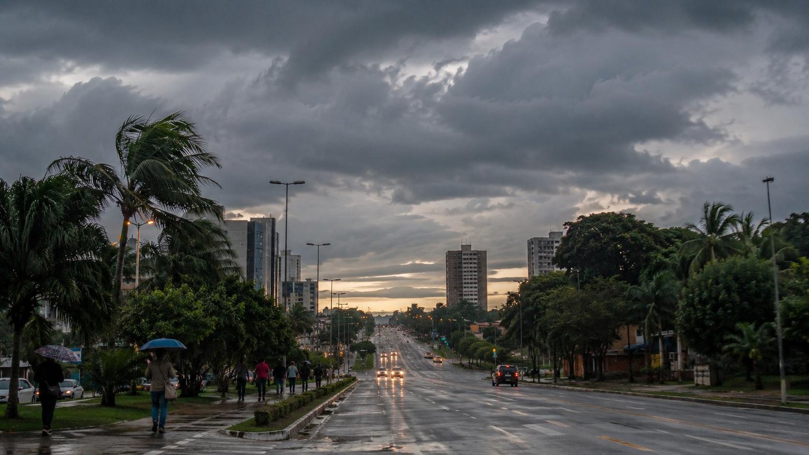 Avenida sob nuvens carregadas em Rondônia com pista molhada, pedestres e cenário de chuva