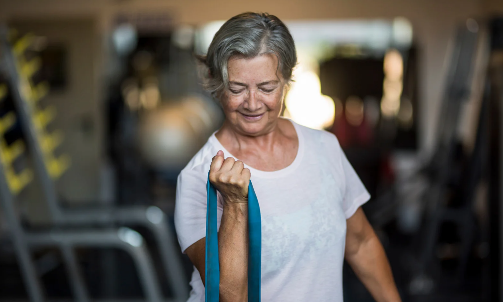 Mulher idosa fazendo atividade física com faixa elástica, ilustrando exercício no horário certo e saúde do coração.