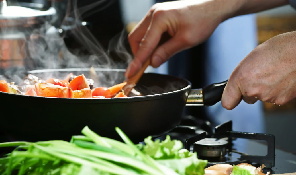 Mãos preparando legumes em uma panela, imagem sobre estudo que indica que cozinhar reduz risco de demência