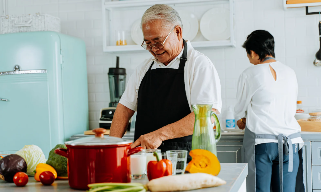 Idosos preparando refeição em cozinha clara, imagem sobre estudo que mostra que cozinhar reduz risco de demência