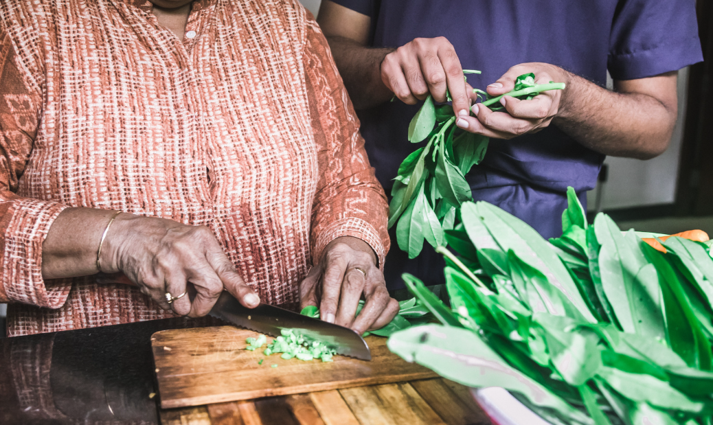 Pessoa idosa cortando legumes e folhas verdes, imagem sobre estudo que indica que cozinhar reduz risco de demência