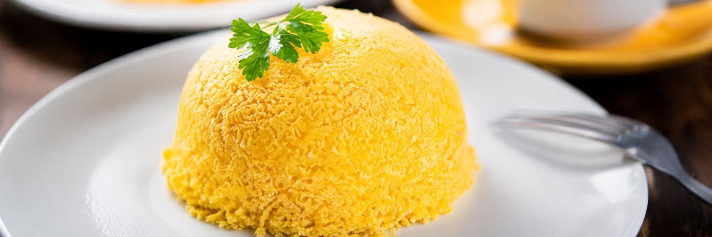 Cuscuz de milho em prato branco com salsinha, em imagem horizontal otimizada para capa de artigo sobre saúde intestinal.