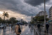 Frente fria no Brasil provoca chuva e queda de temperatura Frente fria no Brasil provoca chuva em avenida urbana com pessoas usando guarda-chuvas e céu nublado