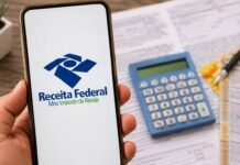 Receita libera primeiro lote do IR com pagamento recorde nesta sexta Celular com tela da Receita Federal em destaque sobre mesa com calculadora e documentos do Imposto de Renda.