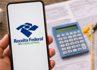 Receita libera primeiro lote do IR com pagamento recorde nesta sexta Celular com tela da Receita Federal em destaque sobre mesa com calculadora e documentos do Imposto de Renda.