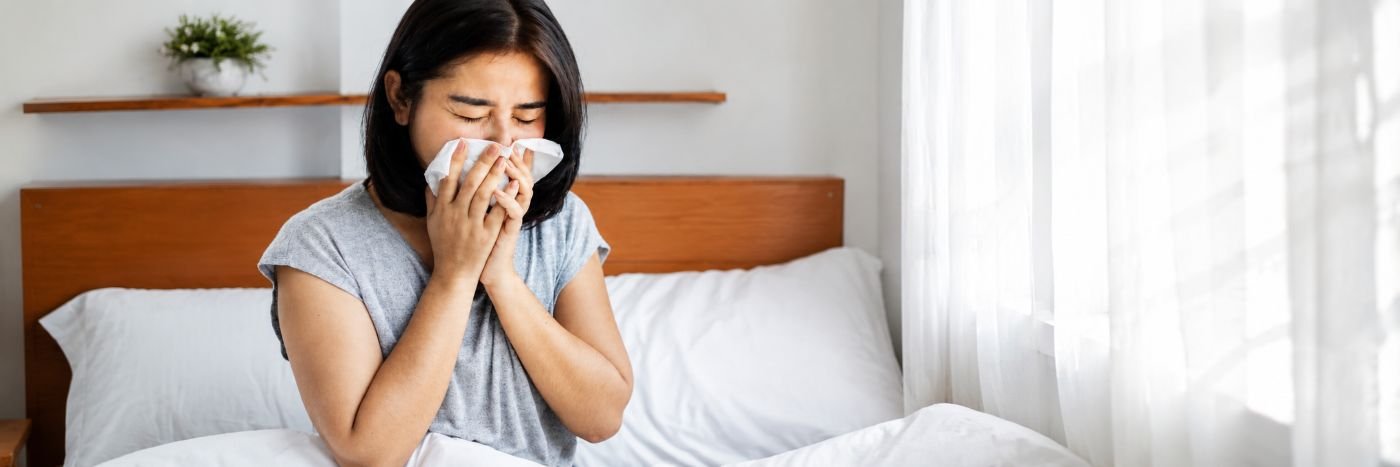 Mulher com sintomas de gripe usando lenço em quarto claro, imagem ilustrativa sobre influenza e cuidados com a saúde