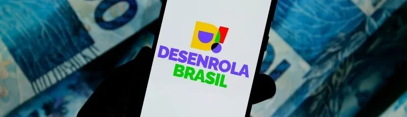 Celular com marca do Desenrola Brasil sobre fundo com cédulas de dinheiro brasileiro