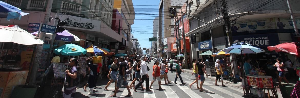 Rua movimentada no centro comercial brasileiro com pedestres atravessando, lojas abertas e comércio popular