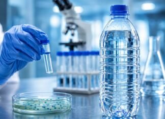 Entenda o risco da Pseudomonas aeruginosa achada em lote de água Garrafa de água mineral em bancada de laboratório durante análise sanitária relacionada à Pseudomonas aeruginosa