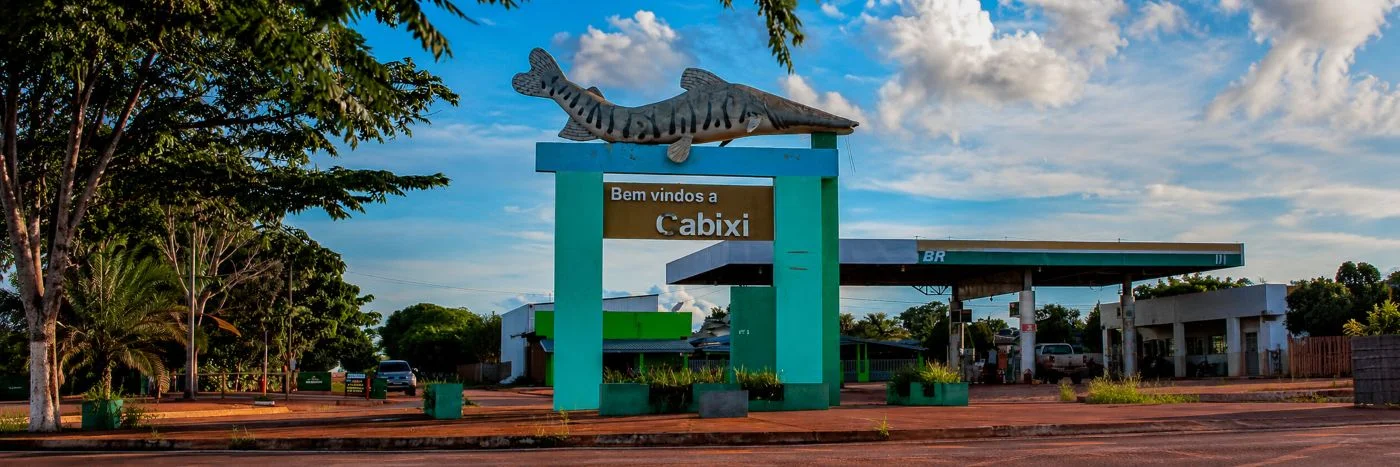 Imagem-faixa mostra pirarucu na merenda escolar com alimentos regionais e estudantes em refeitório.