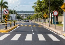 Candeias abre pregão de R$ 6,39 milhões para sinalização viária Imagem ilustrativa de sinalização viária com faixa de pedestres, placas e lombada em uma rua urbana.