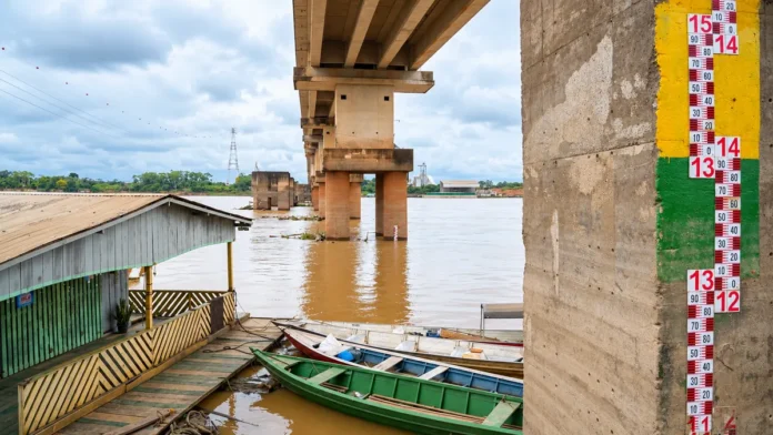Composição visual baseada em fotografia fornecida pelo editor mostra o nível do Rio Madeira, régua fluviométrica, ponte e embarcações em Porto Velho.