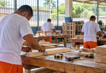 Rondônia ocupa 3º lugar nacional em participação no trabalho prisional Cena ilustrativa de trabalho prisional em Rondônia, com adultos realizando atividades de marcenaria em oficina.