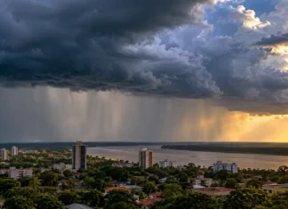 Inmet prevê chuva e trovoadas em Rondônia até Finados Composição ilustrativa de nuvens carregadas e chuva distante sobre cidade próxima a um rio, para notícia sobre chuva em Rondônia.