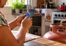 MDS esclarece boatos sobre cortes no Bolsa Família e Gás do Povo Imagem ilustrativa de pessoa consultando o celular na cozinha ao lado de botijão de gás.